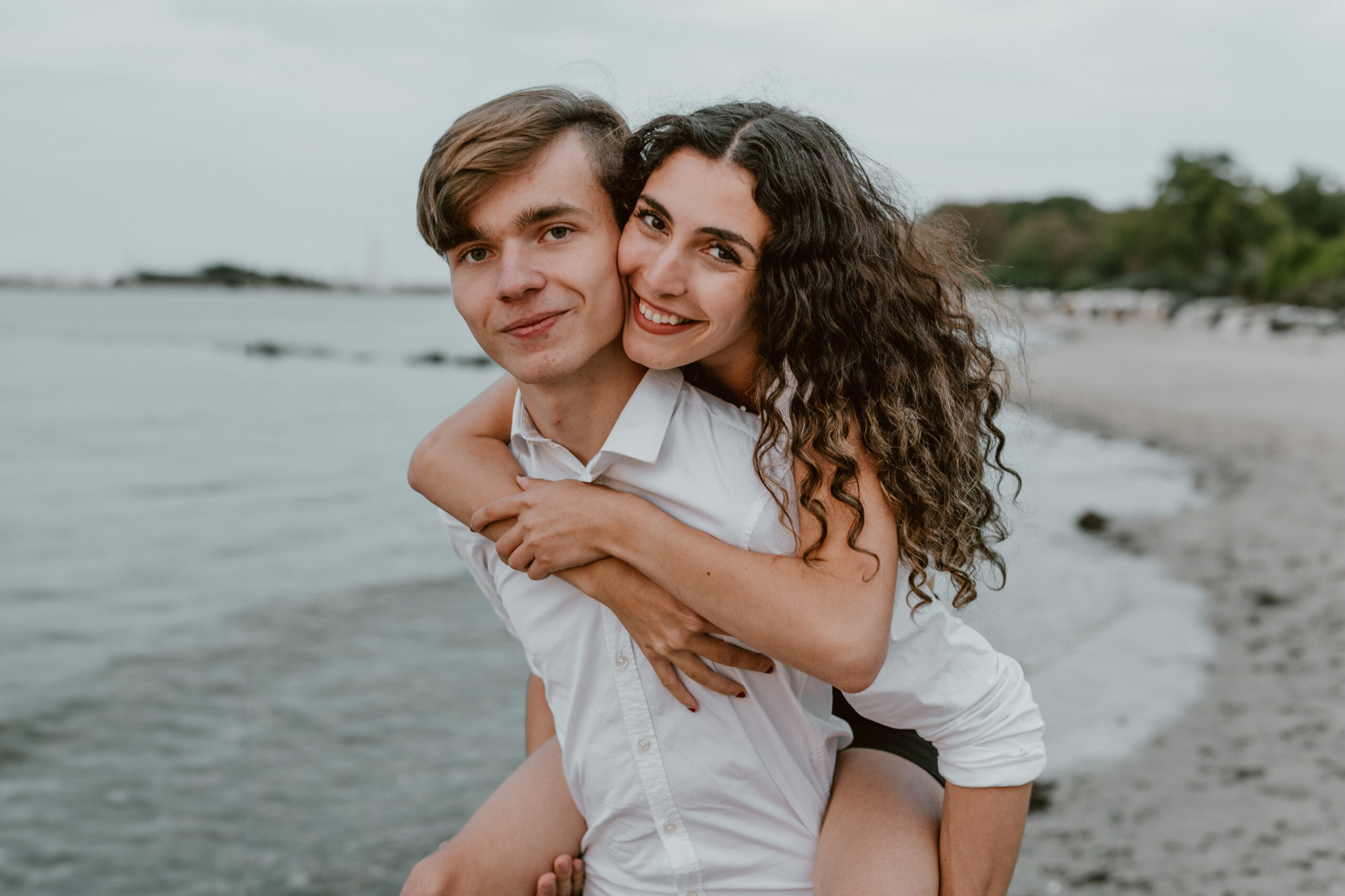Paarfotografie: Ein Paar umarmt sich liebevoll und schaut sich dabei vertraut am Timmendorfer Strand an.